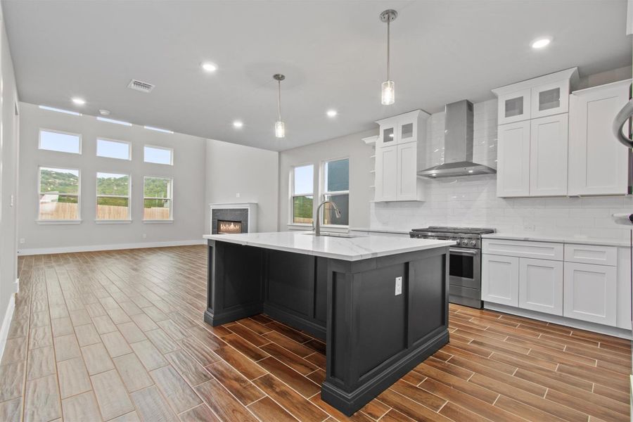 Kitchen featuring decorative light fixtures, white cabinetry, high end range, and wall chimney exhaust hood