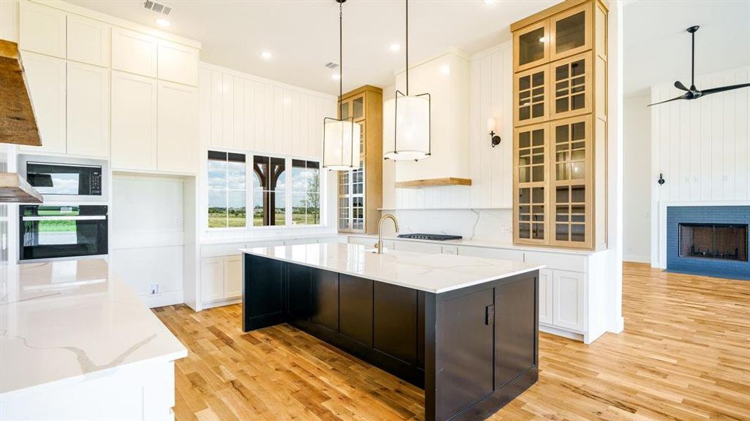 Kitchen with black appliances, an island with sink, light stone counters, and white cabinetry