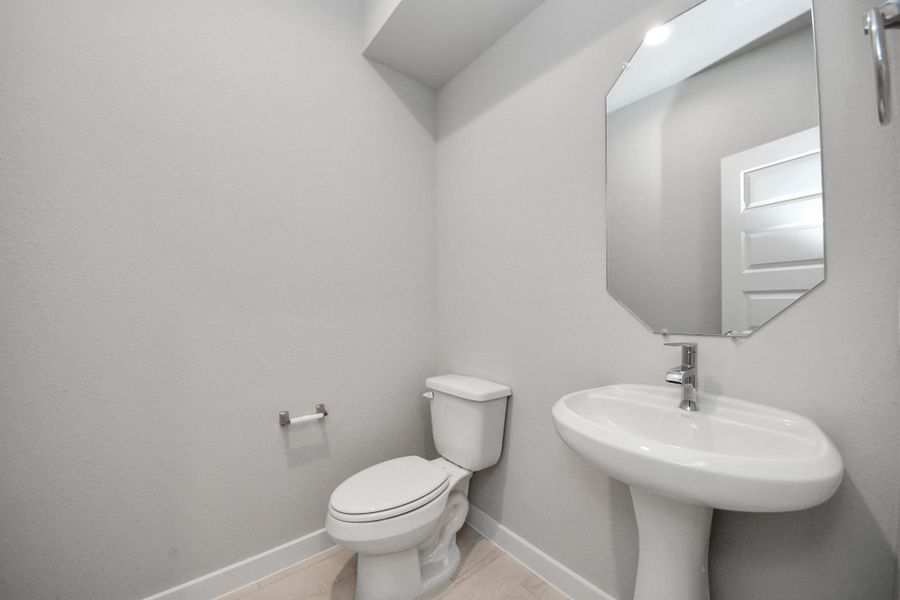 This half bathroom features a stylish pedestal sink, modern hardware, and bright recessed lighting, creating a sleek and inviting space. Sample photo of completed home with similar floor plan. Actual colors and selections may vary.