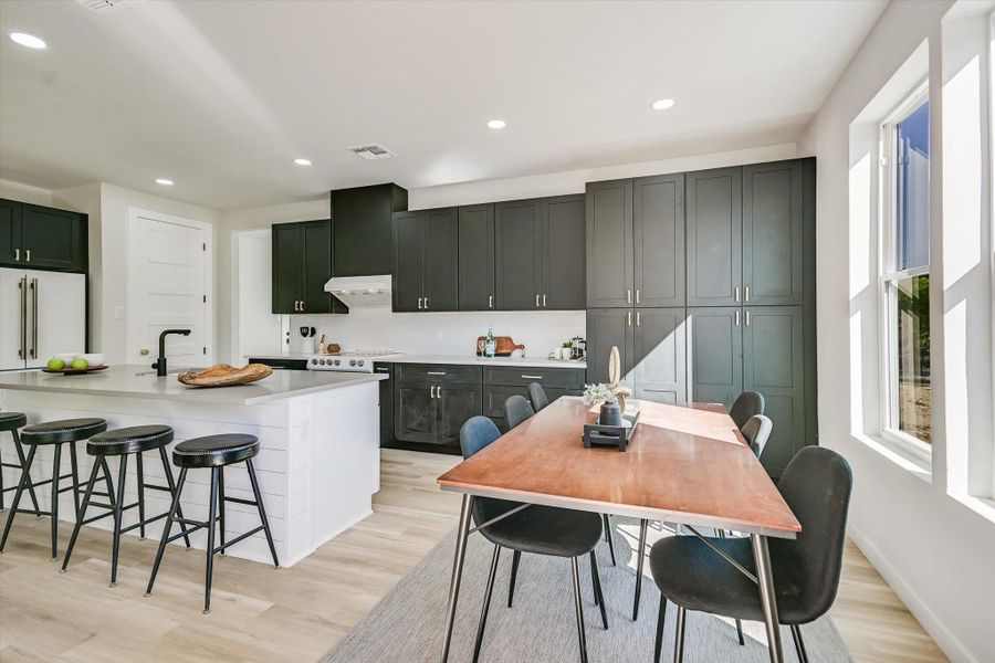 Kitchen with recessed lighting, a kitchen bar, light wood-type flooring, a center island with sink, and high end refrigerator