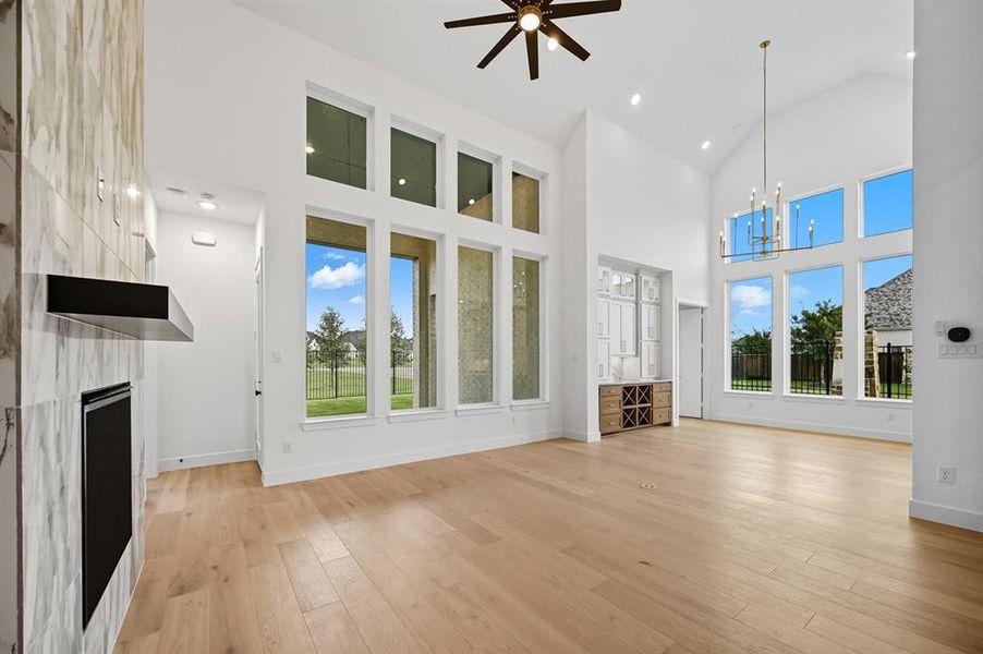 Unfurnished living room featuring high vaulted ceiling, a chandelier, light wood finished floors, a high end fireplace, and a ceiling fan Unfurnished living room featuring high vaulted ceiling, a chandelier, light wood finished floors, a high end fireplace, and a ceiling fan