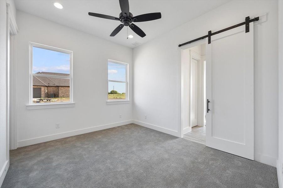 Secondary bedroom with a barn door, carpet flooring, recessed lighting, and baseboards Secondary bedroom with a barn door, carpet flooring, recessed lighting, and baseboards