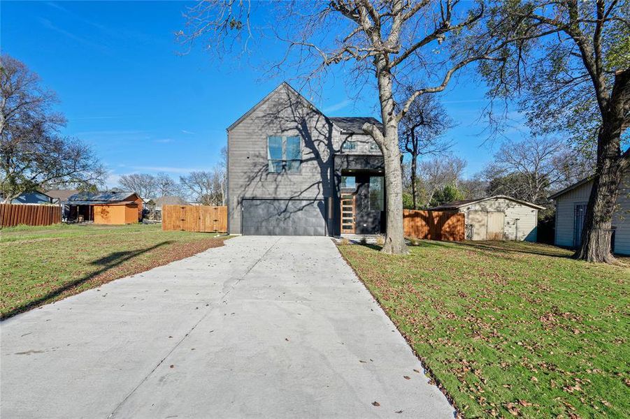 View of front of house with concrete driveway, a storage shed, and an attached garage