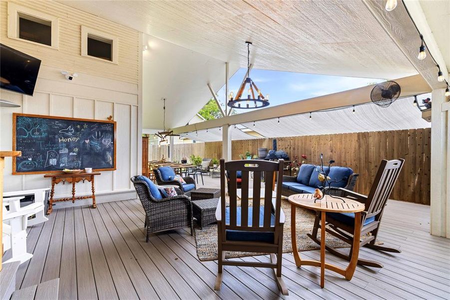Expansive covered patio featuring wood-finish decking, a vaulted ceiling, string lighting, and a privacy fence