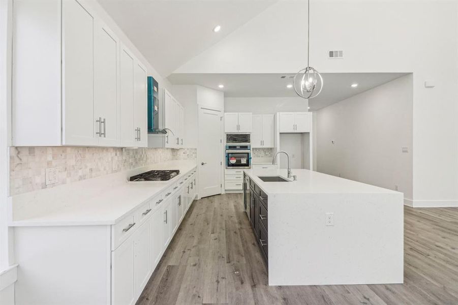 Kitchen featuring white cabinetry, decorative backsplash, hanging light fixtures, light stone counters, and light wood-type flooring