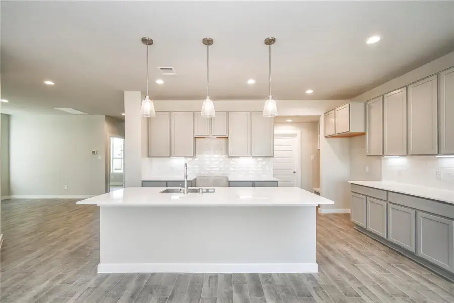 Step into a dream realized with this generously spacious kitchen! A massive granite island takes center stage, complemented by high ceilings, soft-close cabinets, granite countertops, stainless steel appliances, a sleek tile backsplash, and recessed lighting. The extended counter area adds practicality to the stylish design. The open concept effortlessly connects the kitchen to the expansive family room. Sample photo of completed home with similar floor plan. Actual colors and selections may vary.
