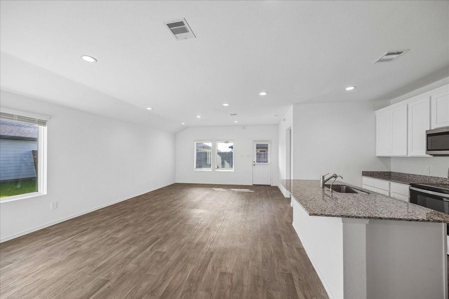 Spacious, open-concept living area with wood flooring and abundant natural light. The kitchen features granite countertops, white cabinetry, and stainless steel appliances, offering a modern and inviting space for cooking and entertaining.
