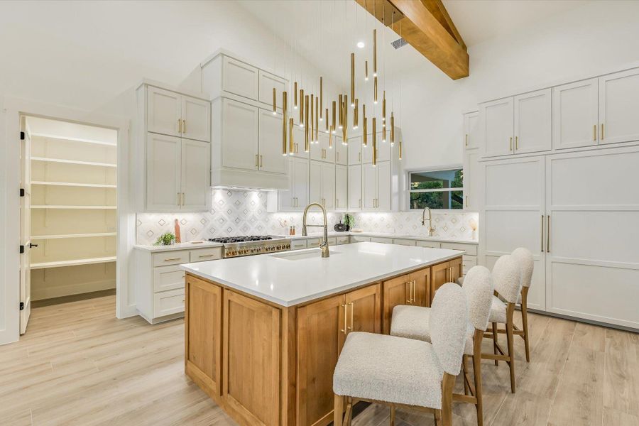 Two tone kitchen featuring dual tone cabinets, a kitchen island with sink, light wood finished floors, decorative backsplash, and a kitchen breakfast bar