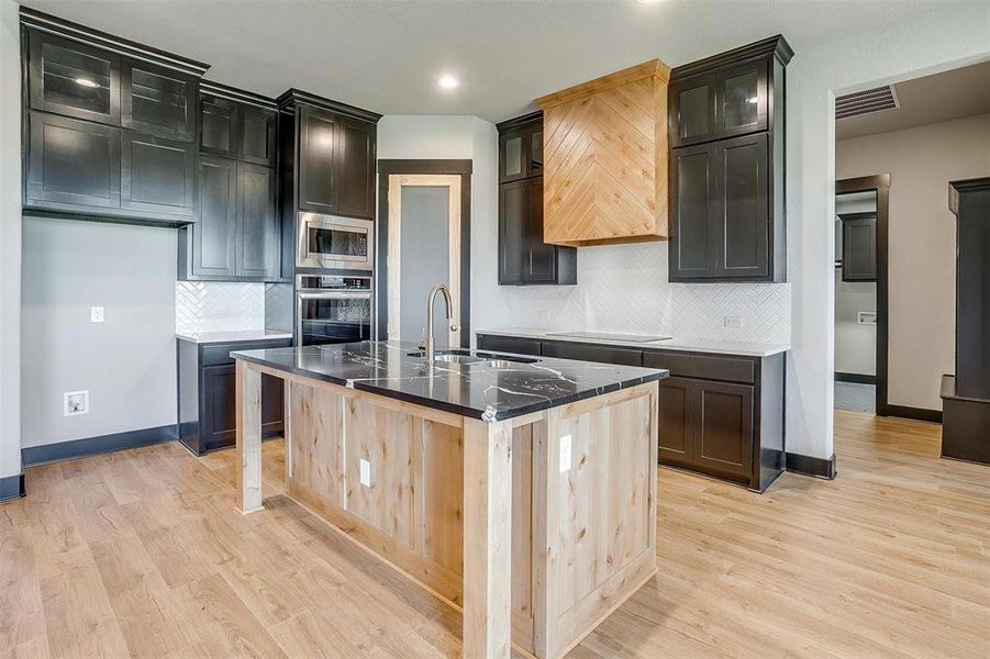 Kitchen featuring decorative backsplash, stainless steel appliances, light hardwood / wood-style flooring, and a kitchen island with sink