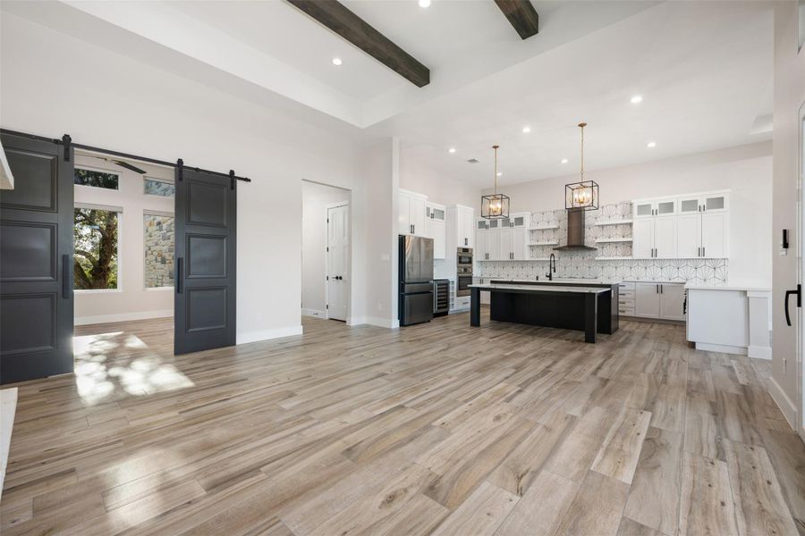 Kitchen with white cabinetry, hanging light fixtures, stainless steel refrigerator, a center island with sink, and a barn door
