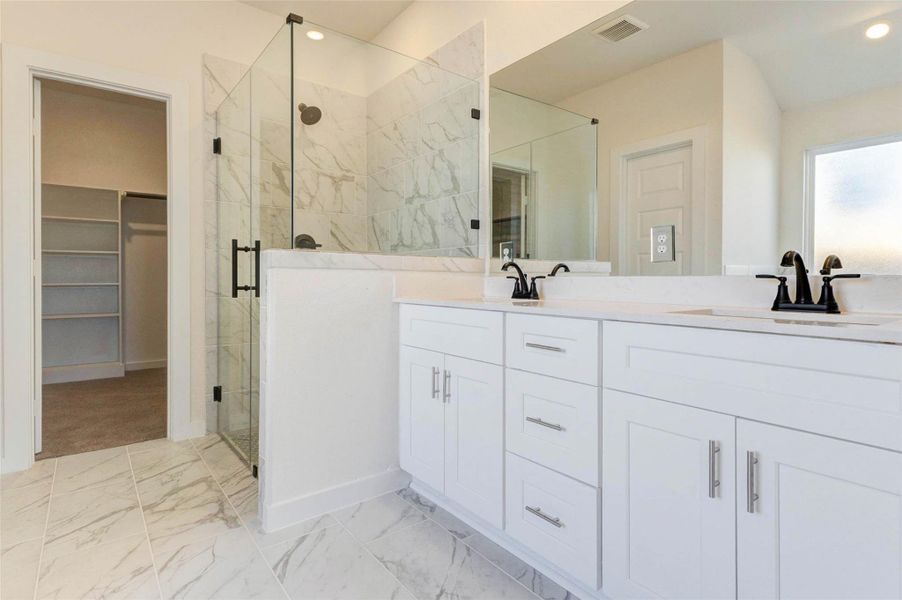 Spacious primary bathroom featuring a sleek double-sink vanity with quartz countertops, crisp white cabinetry, and modern hardware. The oversized glass-enclosed walk-in shower is finished with elegant marble-style tile and matte black fixtures, offering a spa-like experience. Large mirrors and recessed lighting keep the space bright and airy, while the thoughtful layout provides ample storage and comfort for daily routines.
