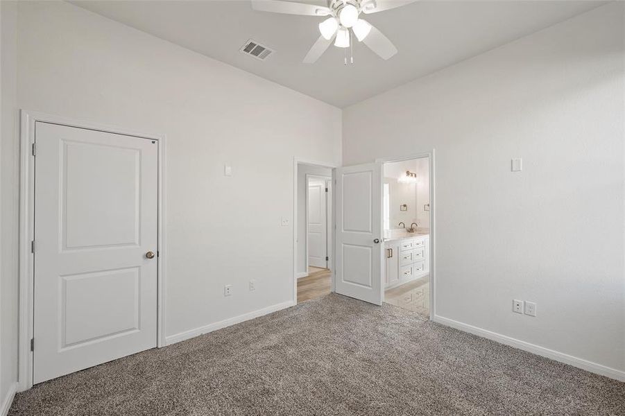 Unfurnished bedroom with light carpet, ceiling fan, and connected bathroom