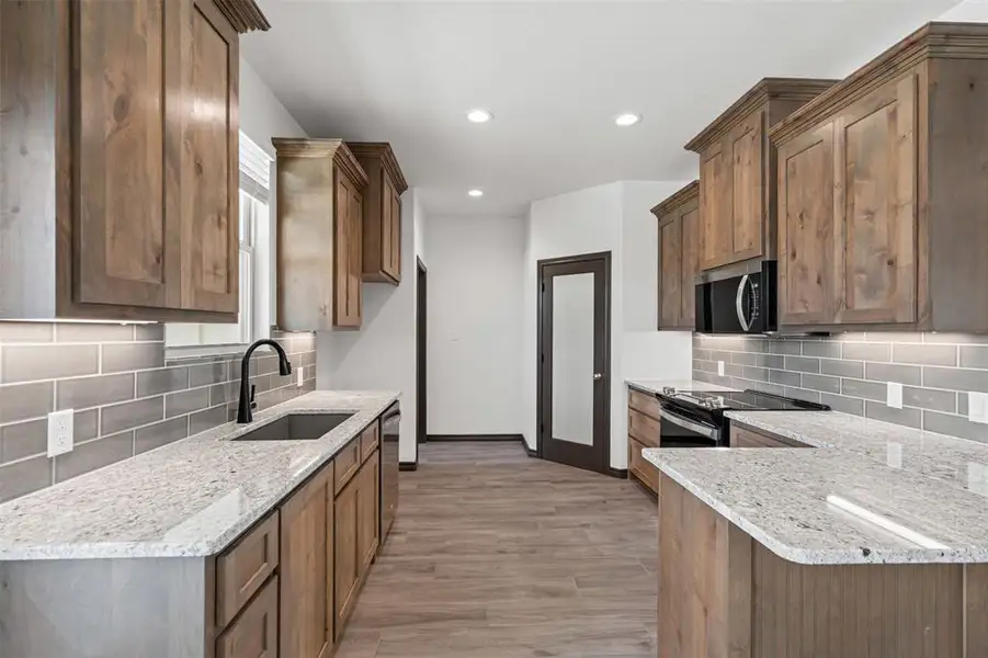 Kitchen with backsplash, light wood finished floors, light stone counters, recessed lighting, and stainless steel appliances