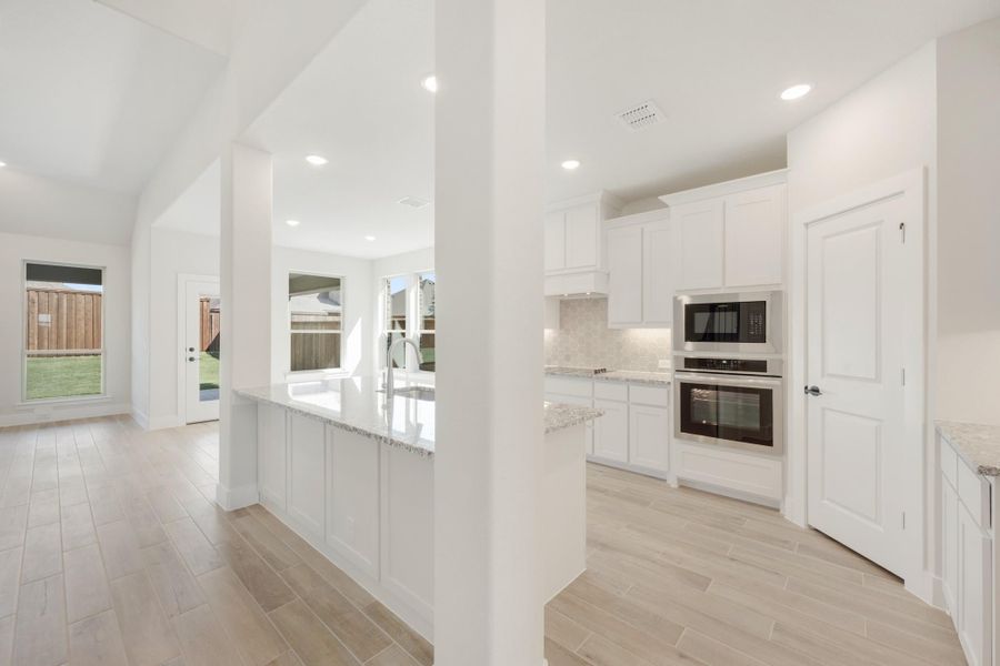 Open kitchen with white cabinets, granite island, stainless steel appliances, and light wood-look tile floors