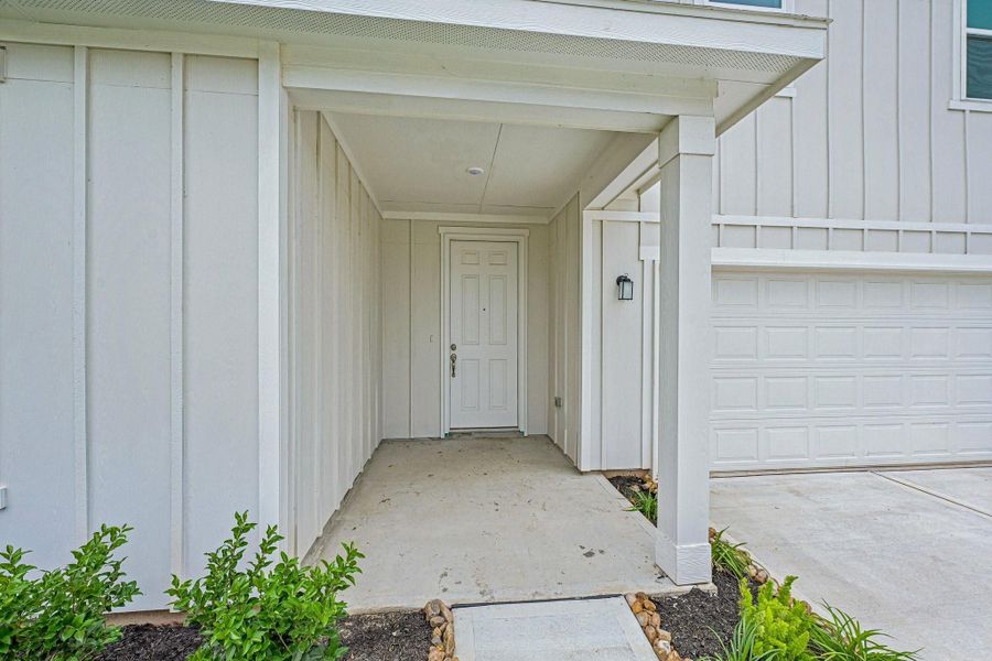 A welcoming large covered front patio sets the tone with clean architectural lines, a rich wood front door, and landscaped garden beds that create inviting curb appeal.