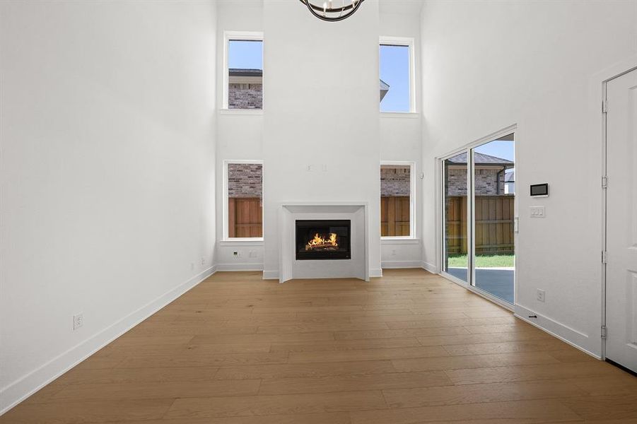 Unfurnished living room featuring healthy amount of natural light, a towering ceiling, a warm lit fireplace, and wood-type flooring
