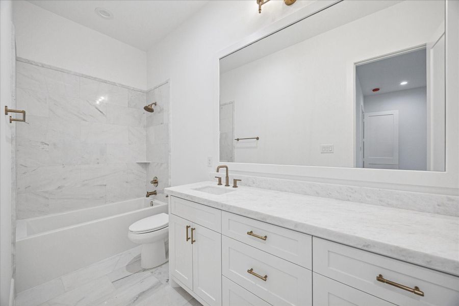 Marble surrounds the tub shower combination, paired with a wide vanity, soft brass plumbing, and abundant lighting. A calm, elevated environment for guests or family. Marble surrounds the tub shower combination, paired with a wide vanity, soft brass plumbing, and abundant lighting. A calm, elevated environment for guests or family.
