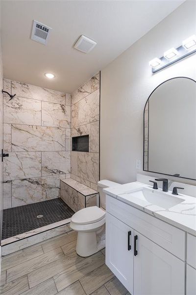 Bathroom featuring toilet, a tile shower, and vanity