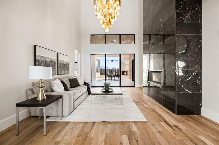 Living room with a towering ceiling, a fireplace, hardwood / wood-style floors, and a notable chandelier