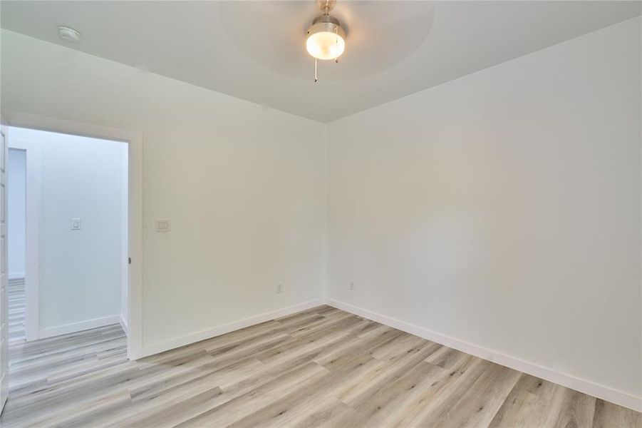 Interior room featuring light wood-finish flooring, white walls, and a ceiling fan with integrated lighting