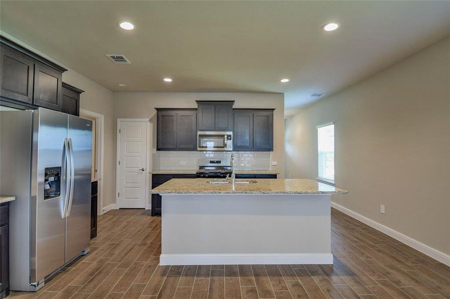 Kitchen featuring appliances with stainless steel finishes, an island with sink, dark wood-style flooring, decorative backsplash, and recessed lighting Kitchen featuring appliances with stainless steel finishes, an island with sink, dark wood-style flooring, decorative backsplash, and recessed lighting
