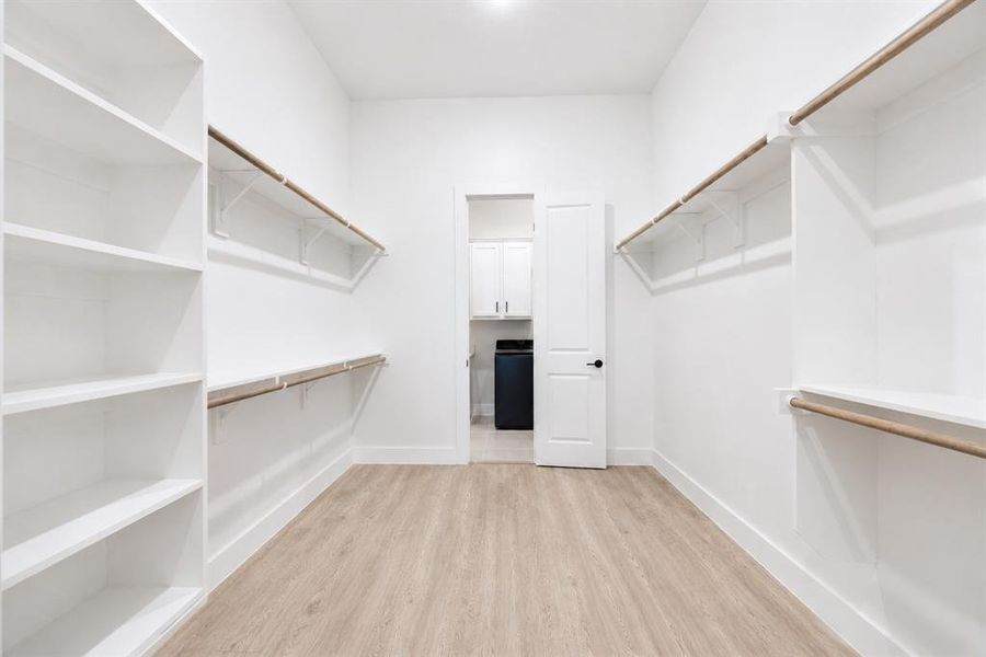 Spacious walk-in closet featuring light wood-finish flooring, white walls, and recessed lighting