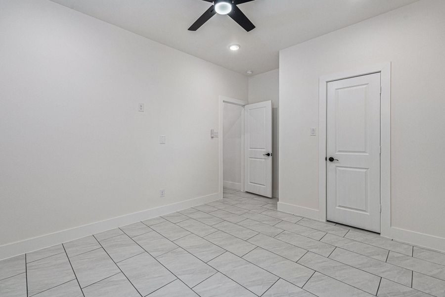 This room features clean white walls, tiled flooring, and a ceiling fan. It has two doors, offering potential for storage or access to other areas, creating a bright and versatile space.