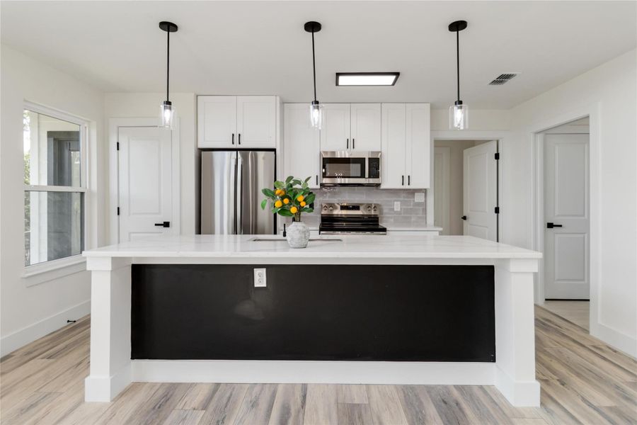 Chef’s kitchen featuring a large center island, stainless steel appliances, and shaker-style white cabinets with black handles that coordinate with the door hardware Chef’s kitchen featuring a large center island, stainless steel appliances, and shaker-style white cabinets with black handles that coordinate with the door hardware