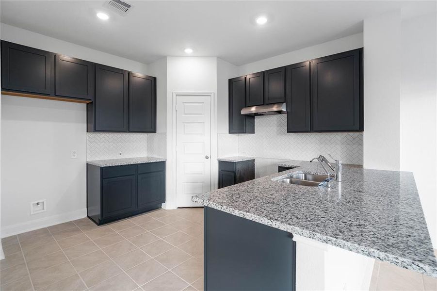 This spacious kitchen features high ceilings, stained wood cabinets, granite countertops, SS appliances, modern tile backsplash, recessed lighting, extended countertop for breakfast bar, and pantry all overlooking your huge family room