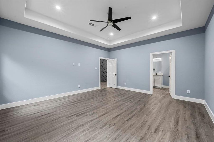 Unfurnished bedroom with a raised ceiling, ceiling fan, light hardwood / wood-style flooring, and ensuite bathroom