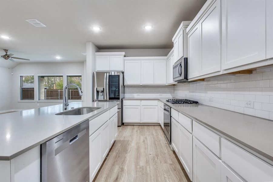Kitchen with appliances with stainless steel finishes, white cabinets, light wood-style flooring, a kitchen island with sink, and recessed lighting Kitchen with appliances with stainless steel finishes, white cabinets, light wood-style flooring, a kitchen island with sink, and recessed lighting