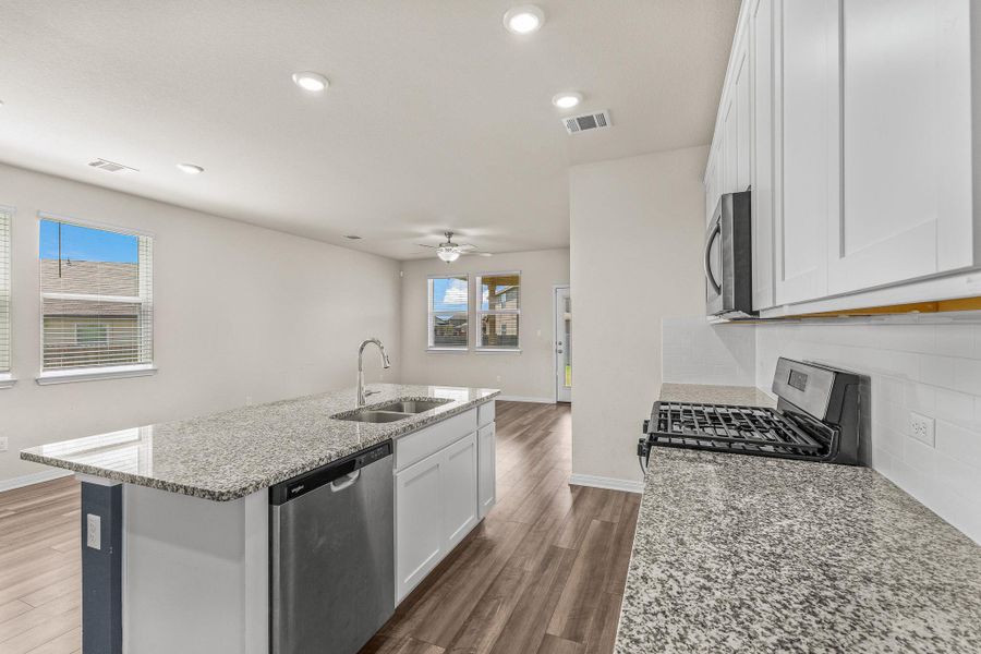 Kitchen featuring white cabinetry, light stone counters, appliances with stainless steel finishes, dark wood finished floors, and a center island with sink Kitchen featuring white cabinetry, light stone counters, appliances with stainless steel finishes, dark wood finished floors, and a center island with sink