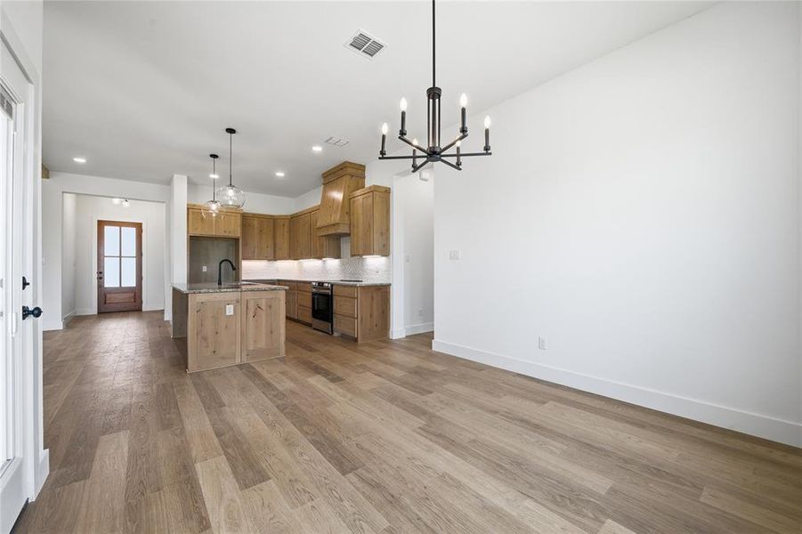 Kitchen featuring open floor plan, stainless steel electric range, a center island with sink, and light wood finished floors Kitchen featuring open floor plan, stainless steel electric range, a center island with sink, and light wood finished floors