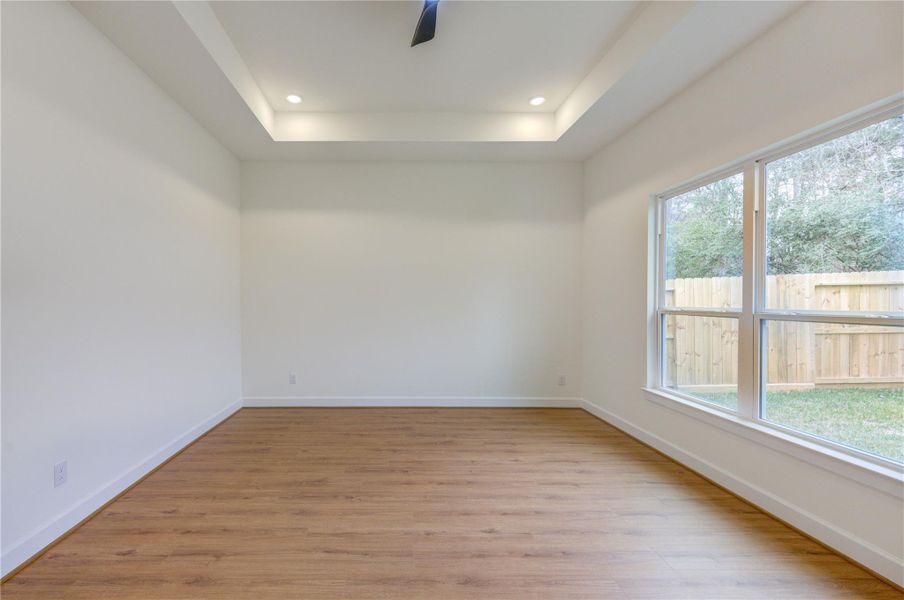 This bright and inviting bedroom features elegant wood flooring, a stylish tray ceiling with recessed lighting, and large windows . This bright and inviting bedroom features elegant wood flooring, a stylish tray ceiling with recessed lighting, and large windows .