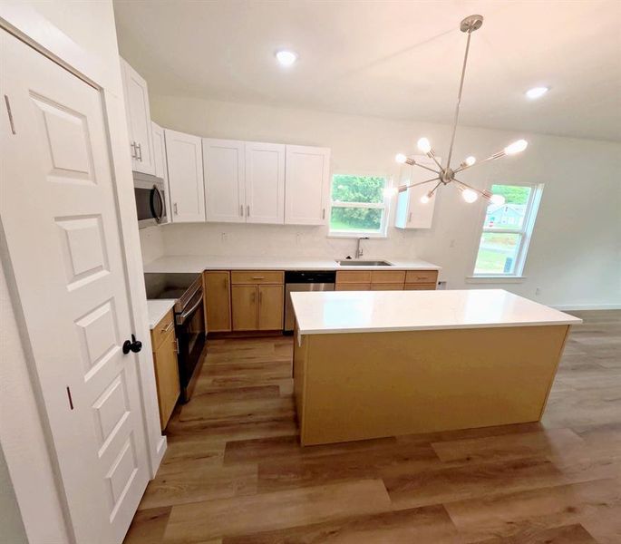 Kitchen featuring white cabinetry, stainless steel appliances, a kitchen island, a chandelier, and light wood-style floors Kitchen featuring white cabinetry, stainless steel appliances, a kitchen island, a chandelier, and light wood-style floors