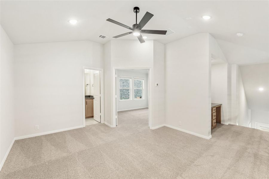 Spacious bedroom with carpet flooring, ceiling fan, and open doorway leading to bathroom and sitting area Spacious bedroom with carpet flooring, ceiling fan, and open doorway leading to bathroom and sitting area