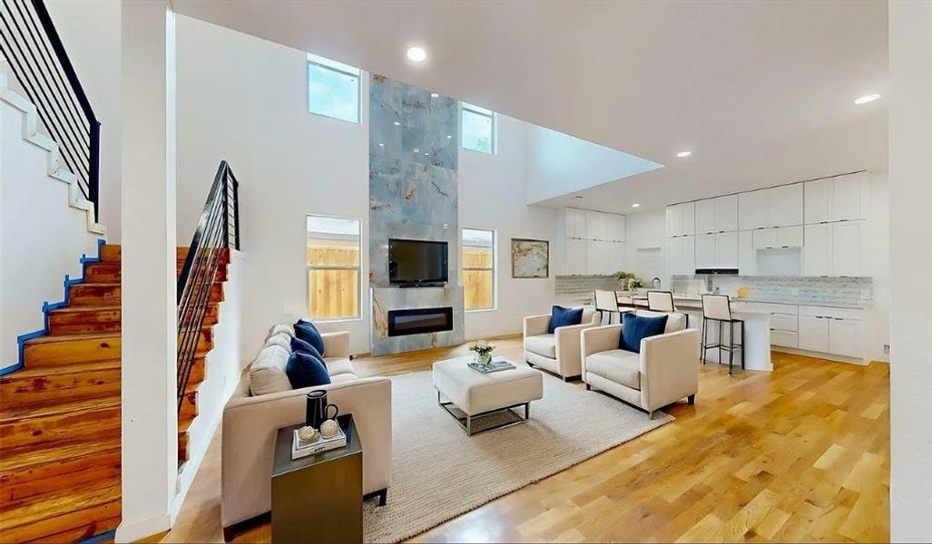 Spacious living area featuring high ceilings, wood-finish flooring, a contemporary fireplace, and a full kitchen with white cabinetry