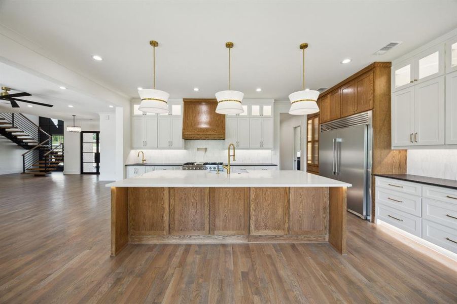 Kitchen with tasteful backsplash, a sink, built in fridge, dark wood-type flooring, and a large island with sink Kitchen with tasteful backsplash, a sink, built in fridge, dark wood-type flooring, and a large island with sink