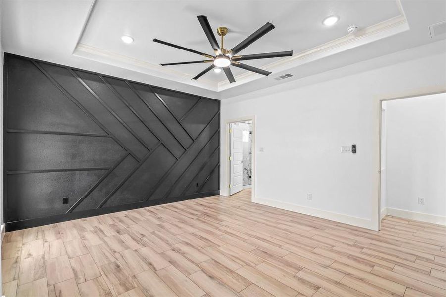 Spare room with light wood-style floors, a decorative wall, ceiling fan, a tray ceiling, and crown molding