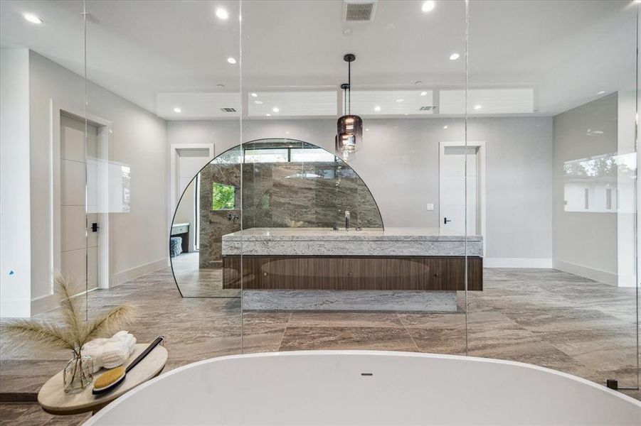 A view reveals the two-sided vanity, each side equipped with a sink, complemented by a curved mirror and vanity lighting. The boutique closet is accessed through two sets of closed doors, offering ample storage and a touch of luxury in this exquisite space.