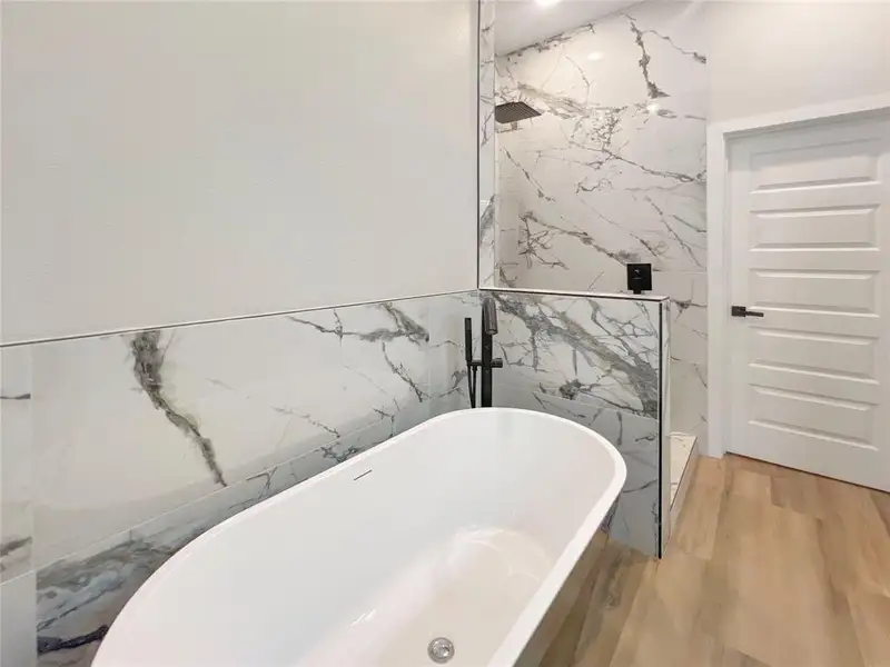 Full bathroom with a freestanding bath, tile walls, wood finished floors, and a marble finish shower Full bathroom with a freestanding bath, tile walls, wood finished floors, and a marble finish shower