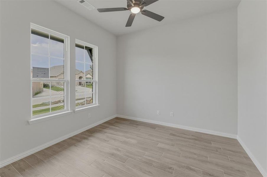 Bright interior space featuring two large windows, wood-finish flooring, a ceiling fan, baseboard trim, and light-colored walls