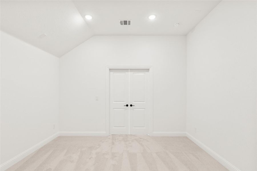 Empty bedroom with vaulted ceiling, light carpet, and white double doors with black handles