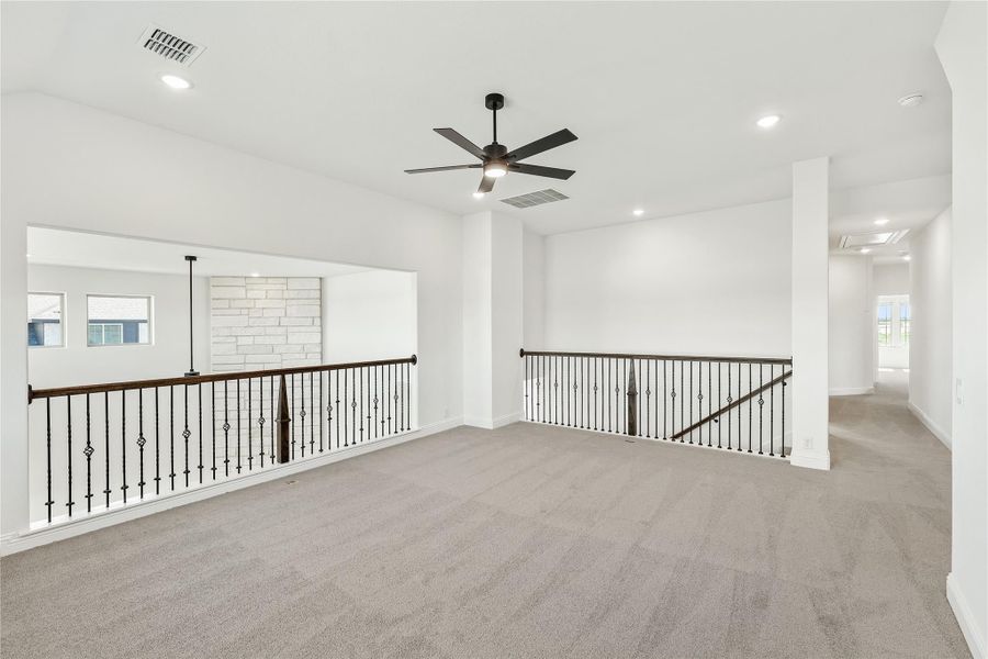 Open upstairs loft with gray carpet, ceiling fan, and iron stair railing overlooking lower level Open upstairs loft with gray carpet, ceiling fan, and iron stair railing overlooking lower level