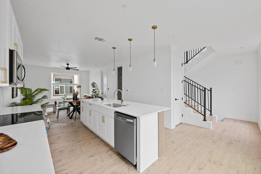 Modern kitchen featuring a large island with white countertops, integrated stainless steel dishwasher, and gold-finish pendant lighting