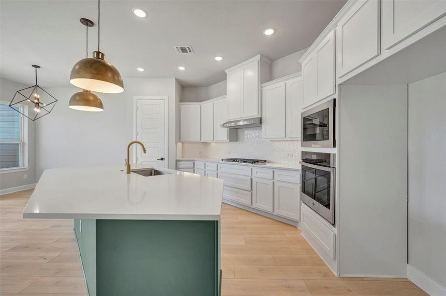 Dual tone kitchen with an island with sink, stainless steel appliances, tasteful backsplash, light wood finished floors, and light stone countertops Dual tone kitchen with an island with sink, stainless steel appliances, tasteful backsplash, light wood finished floors, and light stone countertops