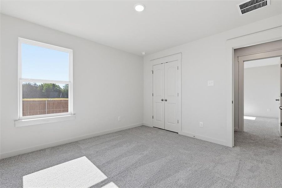 Bright room featuring light gray carpeting, white walls, a single window, and a white bi-fold closet door