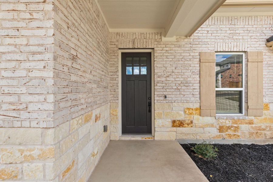 Property entrance featuring brick siding, stone siding, and a porch
