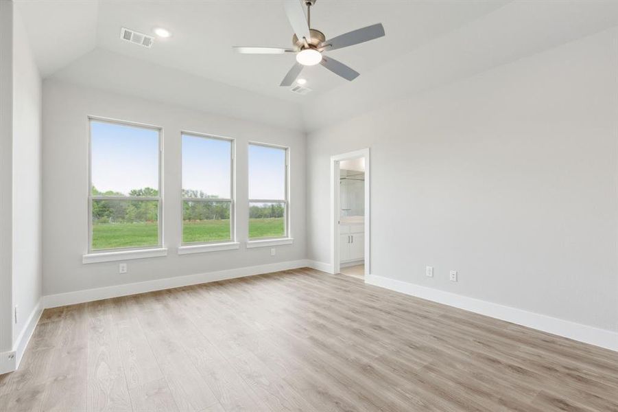 Unfurnished bedroom with multiple windows, light wood-style floors, lofted ceiling, connected bathroom, and a ceiling fan Unfurnished bedroom with multiple windows, light wood-style floors, lofted ceiling, connected bathroom, and a ceiling fan