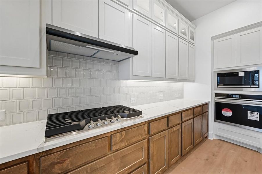 Kitchen featuring backsplash, appliances with stainless steel finishes, light wood finished floors, light stone counters, and range hood Kitchen featuring backsplash, appliances with stainless steel finishes, light wood finished floors, light stone counters, and range hood
